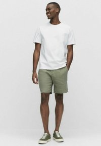 Valkoinen lyhythihainen t-paita, oliivinvihreät shortsit ja oliivinvihreät lenkkarit. Rentoa muotoilua, ei näkyviä kuvioita tai metalliosia.