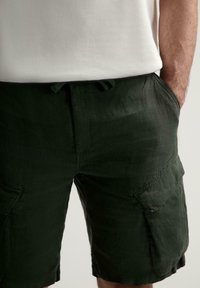 Dunkelgrüne Cargo-Shorts aus strukturiertem Stoff, mit Seitentaschen, einem Kordelzugbund und einer lockeren Passform.