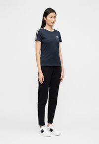 Donkerblauw T-shirt met korte mouwen en contrasterende gestreepte schouderdetails, gecombineerd met zwarte broek en witte sneakers. Eenvoudig en casual ontwerp.