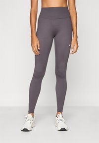 Grå høytlivsleggings med glatt tekstur og elastisk stoff. Har en liten hvit Nike-logo på venstre side. Brukes med hvite joggesko.