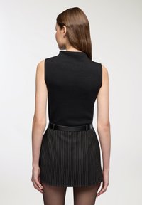 Top nero senza maniche con collo alto, abbinato a una gonna nera a righe sottili. L'outfit presenta una silhouette aderente e una sottile cintura nera.