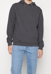 Ciemnoszara bluza z kapturem, długimi rękawami, regulowanym sznurkiem oraz ściągaczami na mankietach i u dołu, połączona z jasnoniebieskimi jeansami.