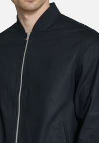 Dark blue bomber jacket, lightweight fabric, ribbed collar, silver zipper, and minimalistic design with side pockets.