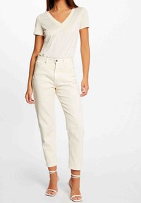 Top beige chiaro a maniche corte con scollatura a V abbinato a pantaloni bianchi a vita alta. I pantaloni presentano una vestibilità slim con chiusura a bottoni e lunghezza cropped.