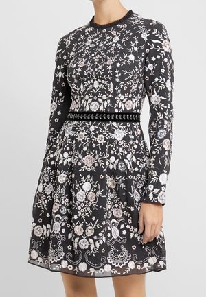 Czarna sukienka z długim rękawem z białym i różowym kwiatowym haftem, dopasowaną talią z czarnym aksamitnym paskiem i marszczonym dekoltem.