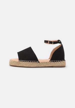 Sandale espadrille en suède noir avec orteils ouverts, bride à la cheville et semelle en jute tissée. Présente des détails cousus le long de la base.