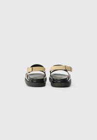 Sandales en daim beige avec une semelle noire. Comprend une bride de cheville avec une boucle, un design plat et un semelle intérieure lisse. Style simple et fonctionnel.