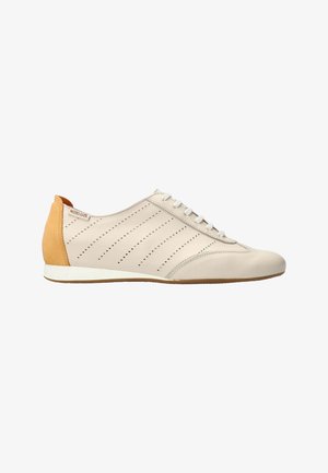 Baskets en cuir beige avec des bandes diagonales perforées, une fermeture à lacets à l'avant, et un panneau talon jaune moutarde sur une semelle blanche.
