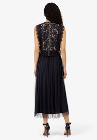 Marineblauwe jurk met een kanten lijfje met getande randen, een tule rok en een verborgen ritssluiting aan de achterkant. Gestyled met hoge hakken.