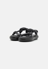 Black sandals featuring a braided upper strap design, soft material, rounded sole, and flat profile for comfort.