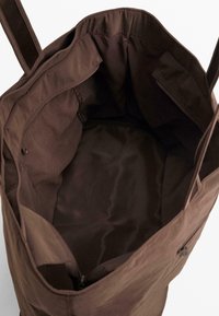 Brown tote bag with a soft, textured fabric, featuring an open top and interior pockets for organization, showcasing a simple, functional design.