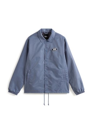 Blauwe nylon coachjack met drukknoopsluiting, elastische manchetten, zijzakken en een centraal logo-embleem. Trekkoord aan de onderrand voor aanpassing.