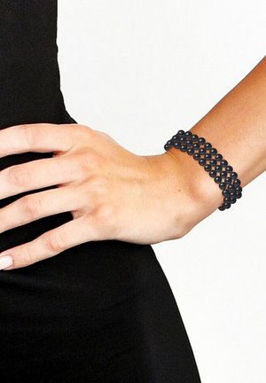 Bracelet noir en perles, composé de perles lisses et mates empilées plusieurs fois, porté au poignet sur un fond sombre.