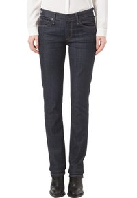 Ciemnoniebieskie dżinsy skinny z średnim stanem, subtelnymi detalami przeszycia i pięcioma kieszeniami, noszone z czarnymi botkami do kostek.