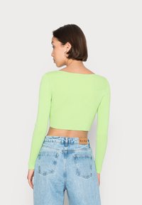 Top cropped de manga longa e canelado em verde néon, combinado com calças de ganga de cintura alta em azul claro com um rótulo na parte de trás.