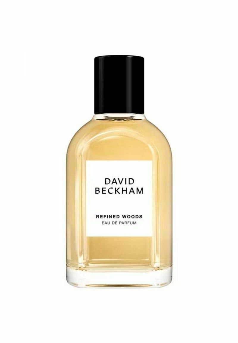 Läpinäkyvä lasipullo pyöreällä muotoilulla, mustalla kannella ja valkoisella etiketillä. Sisältää keltaista nestettä, jonka etiketti on "Refined Woods Eau de Parfum."
