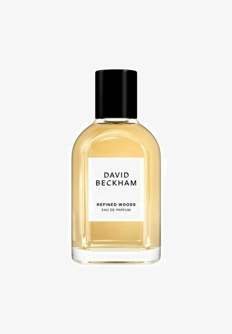 Läpinäkyvä lasipullo pyöreällä muotoilulla, mustalla kannella ja valkoisella etiketillä. Sisältää keltaista nestettä, jonka etiketti on "Refined Woods Eau de Parfum."