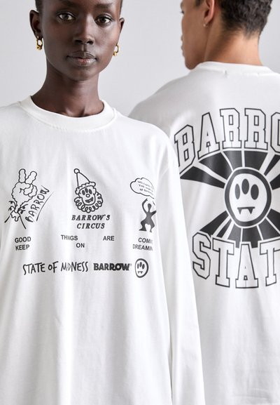 Chemise blanche à manches longues avec des impressions graphiques noires, y compris du texte et des images de dessins animés, à l'avant et à l'arrière, avec des lettres en gras et des motifs.