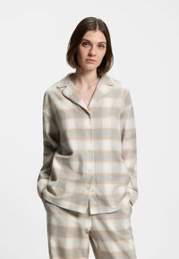 Button-up plaid pajama set in light beige and soft blue, featuring a relaxed fit, collared neckline, and subtle embroidery. Soft fabric texture.