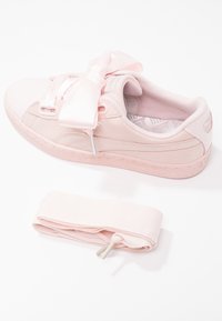 Světle růžová teniska s hladkým a texturovaným povrchem, vybavená objemnými saténovými tkaničkami a vzorovanou stélkou. Obsahuje odpovídající tkaničku.