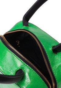 Borsa a mano in pelle verniciata verde con una zip dorata, dettagli neri e due manici. L'interno è in tessuto nero, evidenziando la sua forma strutturata.