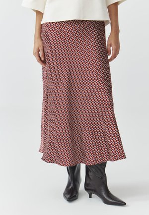 Jupe rouge à motif, avec des formes ovales, fabriquée en tissu léger, dotée d'un ourlet évasé et assortie à des bottines noires à bout pointu.