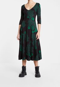 Robe noire mi-longue aux genoux avec imprimé floral vert, col en V et manches trois-quarts, associée à des bottes de combat noires à lacets.