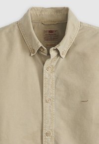 Tan overhemden met een ontspannen kraag, voorzien van beige knopen en gestikte logodetails. Gemaakt van een soepele katoenmix.