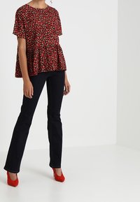 Röd blommönstrad peplum-topp med korta ärmar, i kombination med mörk denim med utsvängda jeans och röda högklackade skor. Slät tygtextur.