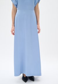 Abito lungo di color azzurro chiaro, caratterizzato da un tessuto testurizzato, maniche corte e larghe, e un taglio dritto, abbinato a scarpe nere a punta.