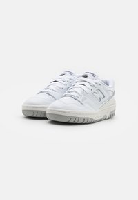 Fehér bőr sneaker, sima textúrával, kiemelkedő ezüst "N" logóval, fűzős kialakítással és vastag, bordás gumitalppal.