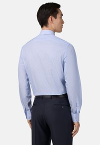 Svetle modrá košile s dlouhým rukávem a vertikálními pruhy, s knoflíkovými manžetami a standardním límcem. Nabaleno s tmavými, dobře padnoucími kalhotami.