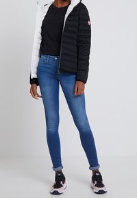 Svart och vit puffjacka med dragkedja, svart t-shirt, blå skinny jeans och rosa-svarta träningsskor med vita sulor.