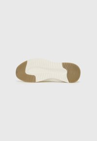Sole of a sneaker, featuring a textured, ivory rubber surface with a tan rubber accent at the toe and grooves for traction.