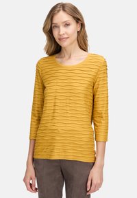 Senfgelbe Drei-Viertel-Ärmel-Bluse mit wellenförmigem Texturmuster, Rundhalsausschnitt und weichem Stoff.