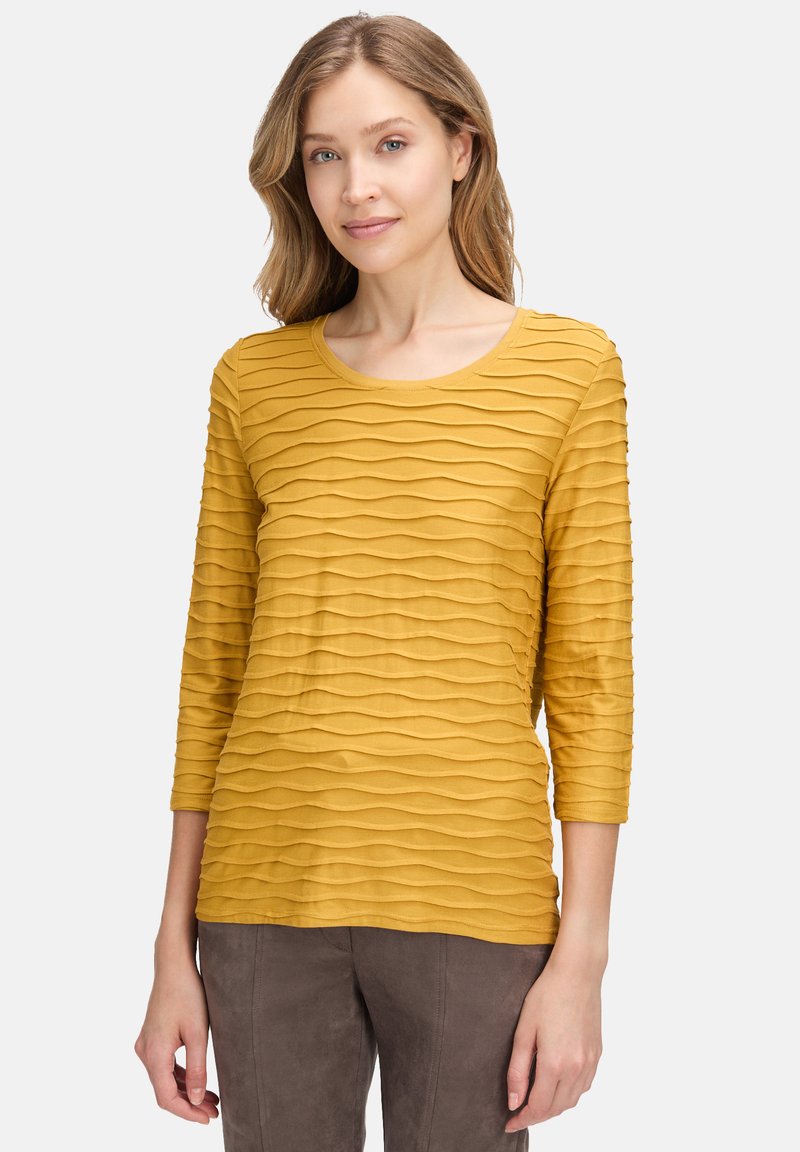 Senfgelbe Drei-Viertel-Ärmel-Bluse mit wellenförmigem Texturmuster, Rundhalsausschnitt und weichem Stoff.