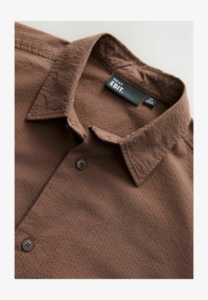Camicia marrone realizzata in tessuto testurizzato, con colletto classico, due bottoni e un'etichetta con "NEXT EDIT."