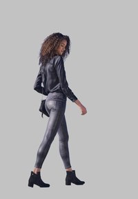 Camicia nera in satin a maniche lunghe abbinata a leggings argentati con motivo. Il modello indossa stivaletti neri alla caviglia; l'outfit presenta una vestibilità slim e un design su misura.