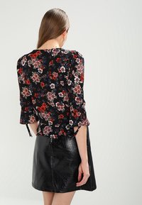 Mustakukkainen paita, jossa on 3/4 hihat, joissa on eloisia punaisia ja valkoisia kukkia, kerättyjä yksityiskohtia ja löysä istuvuus, yhdistettynä kiiltävään mustaan hameeseen.