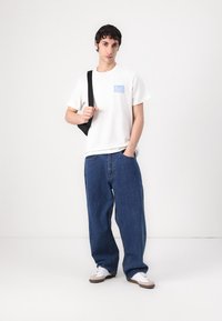 White cotton t-shirt with blue printed text, paired with loose-fitting blue denim jeans. Footwear: white sneakers with brown accents.