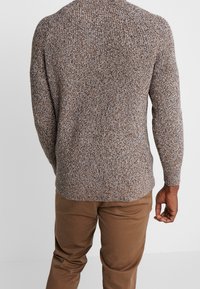 Sweter dziany w odcieniach brązu, beżu i kremu. Charakteryzuje się fakturowanym wykończeniem, długimi rękawami i okrągłym dekoltem. W zestawie z beżowymi spodniami.