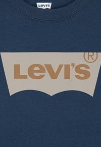 Námořnická modrá tričko s velkým béžovým logem Levi's s zakřiveným designem. Tkanina vypadá hladce a má klasický kulatý výstřih.