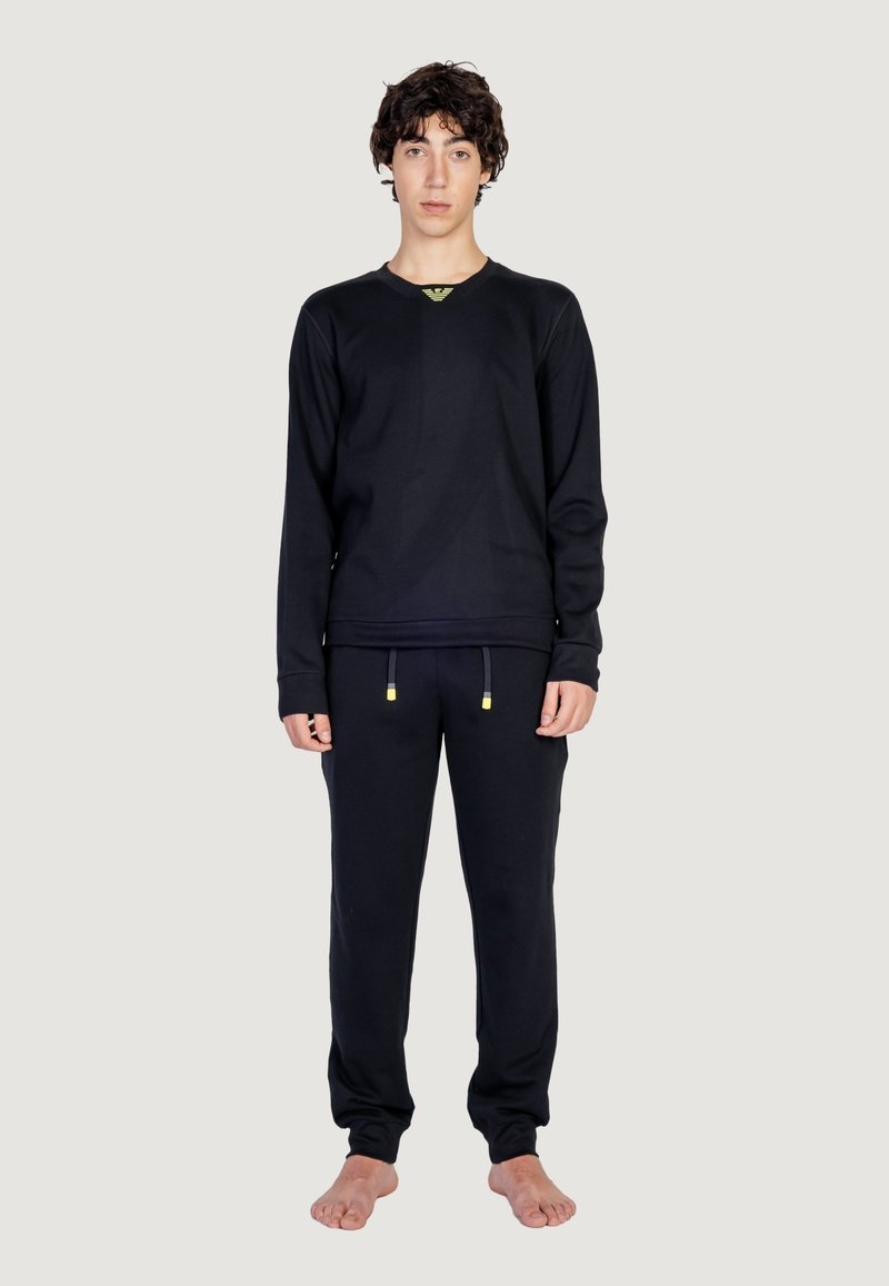 Maglietta nera a maniche lunghe con scollo a V e dettagli gialli, abbinata a pantaloni jogger neri coordinati con coulisse. Nessun motivo visibile.