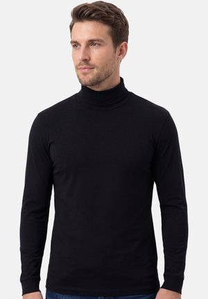 Man met kort bruin haar die een effen zwarte coltrui met lange mouwen draagt, licht naar links kijkend tegen een witte achtergrond.