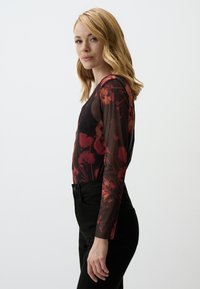Body noir à manches longues avec un design floral transparent dans des tons rouges et foncés, présentant une silhouette ajustée et une texture subtile.