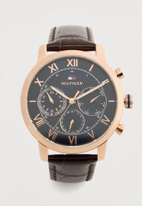 Orologio da polso rotondo con quadrante scuro, cassa in oro rosa, numeri romani, tre sottodial per 24 ore, giorno e data, e cinturino in pelle marrone.