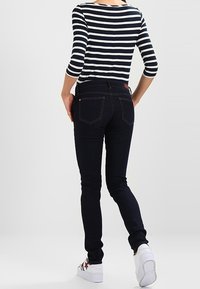 Jeans ajustados de color azul oscuro con una cintura alta, que cuentan con bolsillos traseros y una textura suave, combinados con una blusa a rayas en azul marino y blanco.