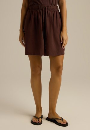 Brązowe, sięgające do kolan szorty z elastycznym pasem i sznurkiem z przodu. Noszone z czarnymi klapkami, posiadającymi płaską podeszwę i cienkie paski.