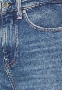 Blå denimjeans med en klassisk femfickdesign, synlig sömnad och knäppning, med en något sliten textur.