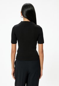 Musta ribbed lyhythihainen polo-toppi, jossa on vartalonmyötäinen muotoilu ja kaulus sekä tekstuuri. Takakuvassa näkyy sileät, saumatonta linjat.